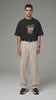 Homme en t-shirt noir imprimé et pantalon beige sur fond gris studio